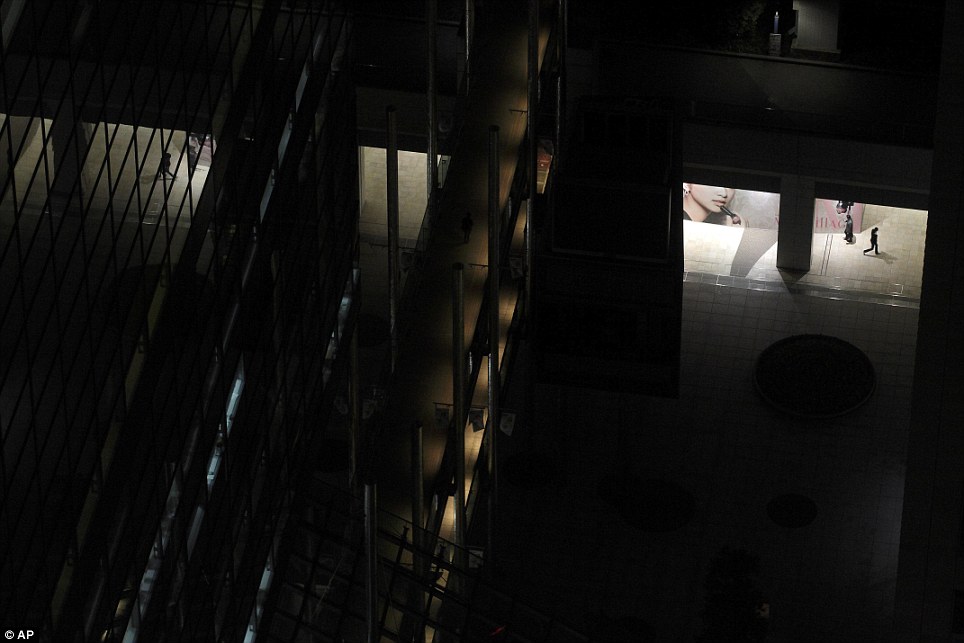 Eerie: People weave their way between blacked out high rises. Tokyo faces at much as six months of blackouts